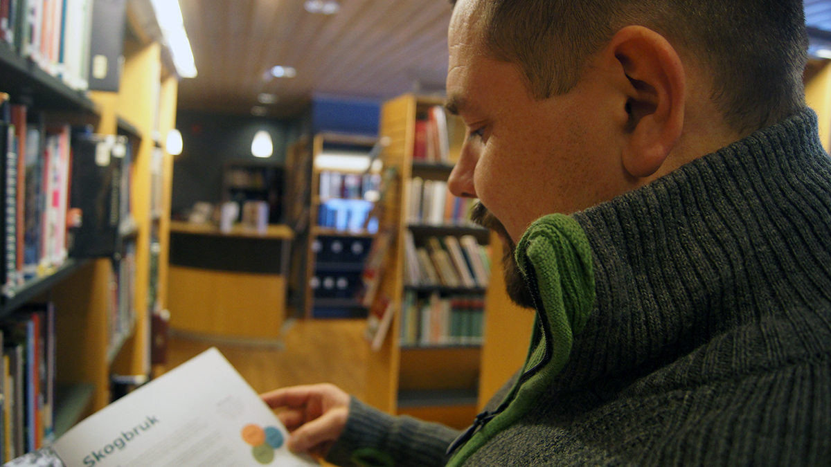 Mann som leser i en bok på et bibliotek
