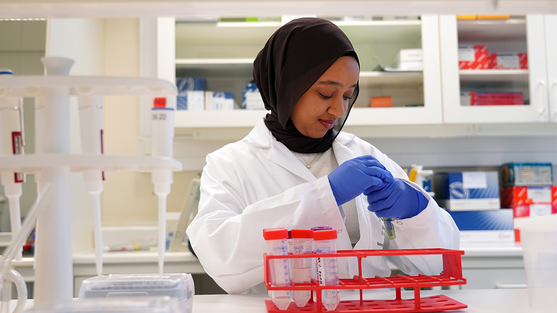 Kvinnelig student i et hvit antrekk på en lab. 