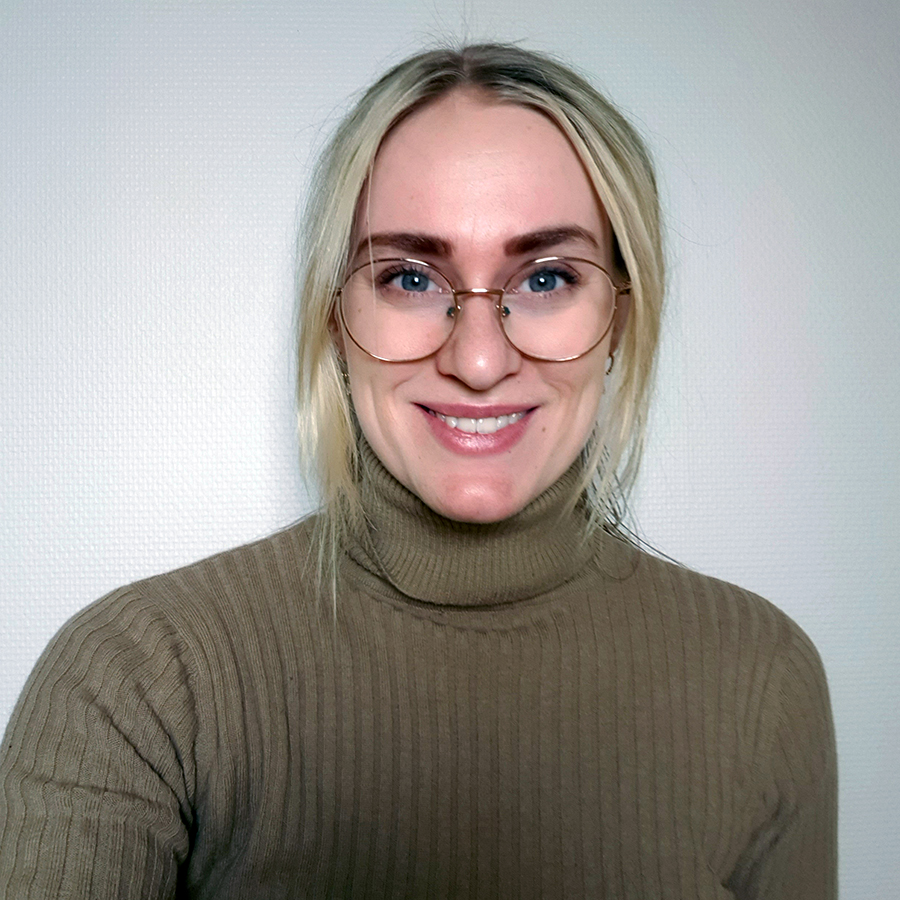 Portrettfoto av student Linnea Paulsen mot en hvit bakgrunn. Hun har på briller og en grønn genser. 