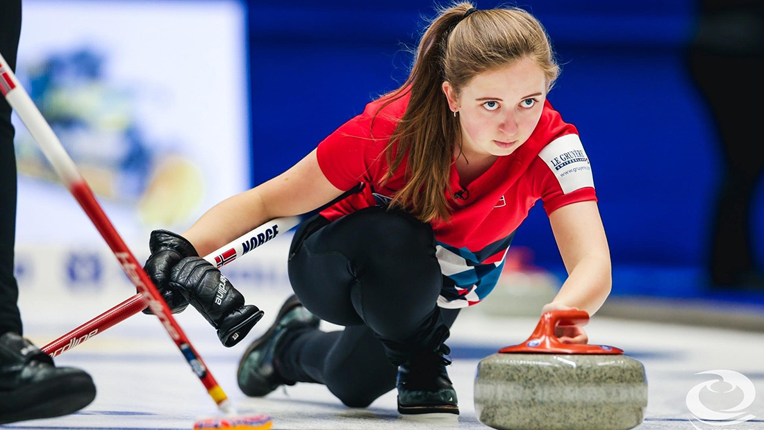 En kvinnelig curlingspiller kledd i rødt som fokuserer på en sten hun skal sende. 